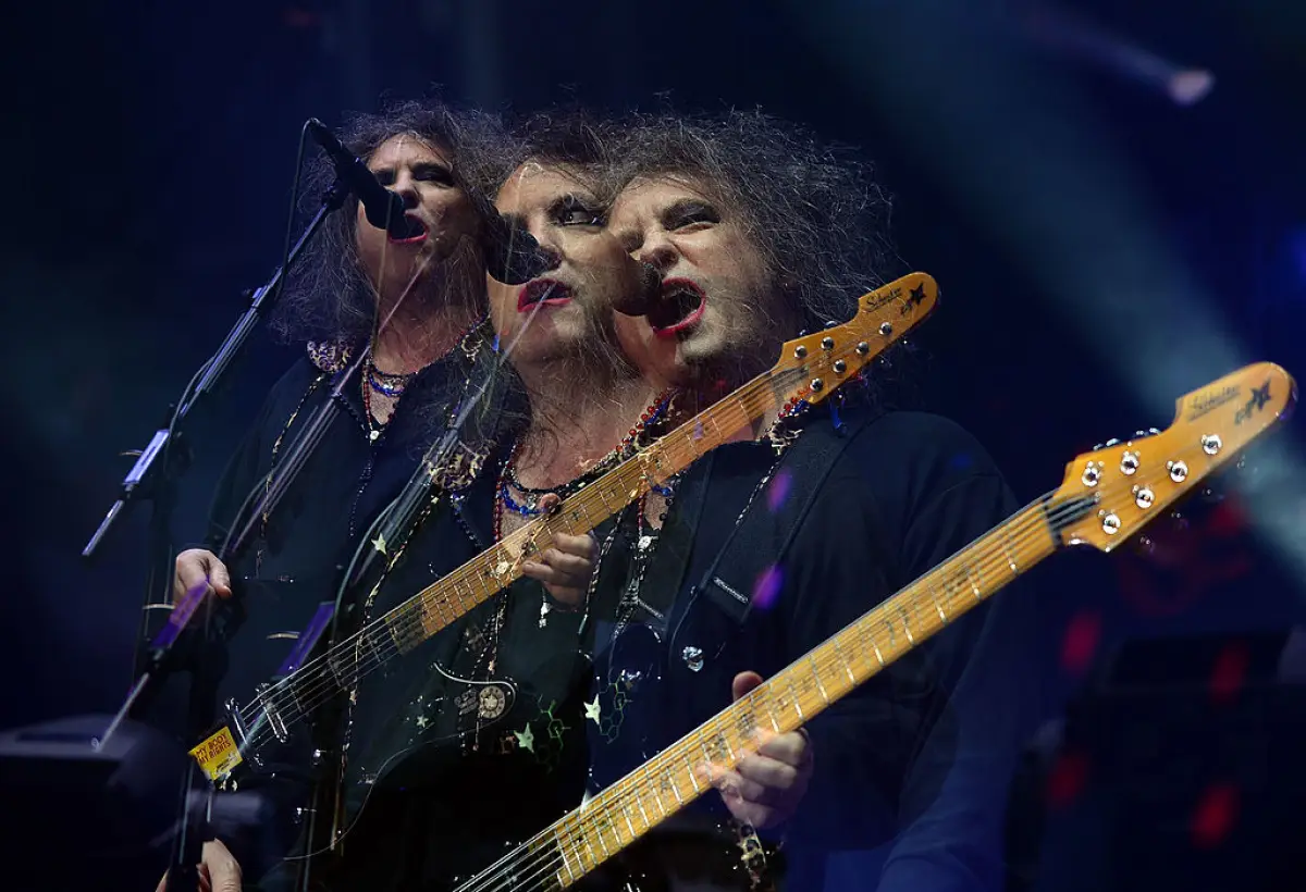 Foto de Robert Smith cantando y tocando la guitarra durante un concierto de The Cure.