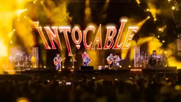 Escenario con las letras Intocable y los músicos con guitarras, acordeón y micrófonos. Hay luces de color amarilla.jpg