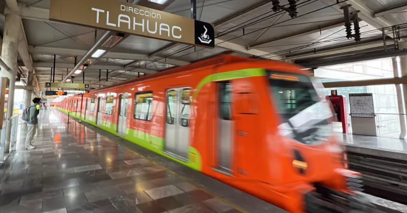Un tren de color naranja con vivos verdes con un letreo que dice Tláhuac, una persona en el anden.jpg