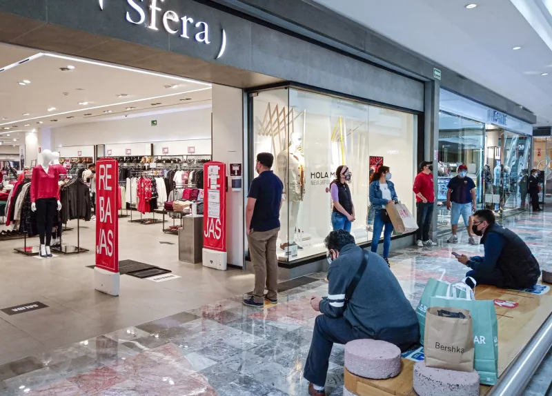 Algunos visitantes realizan filas para ingresar a una tienda de ropa en el centro comercial.