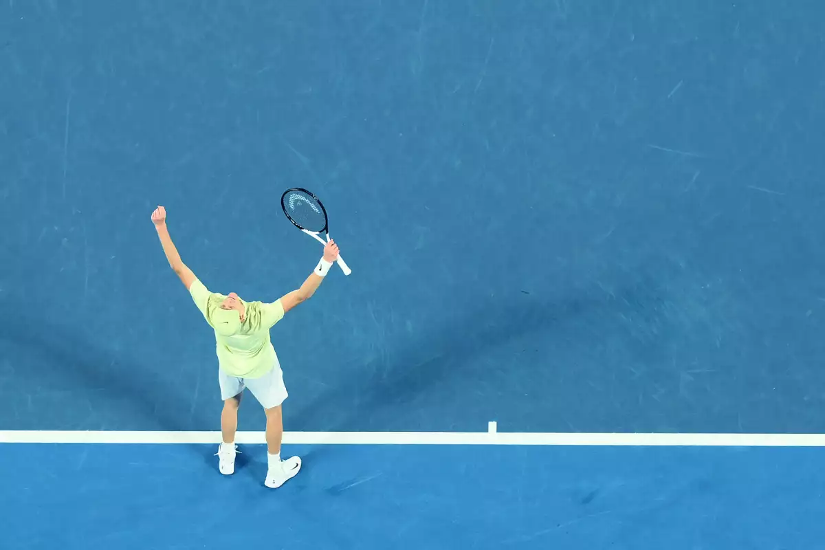 Foto de Jannik Sinner con los brazos levantados y la raqueta en una mano en señal de victoria tras ganar el Abierto de Australia 2025.