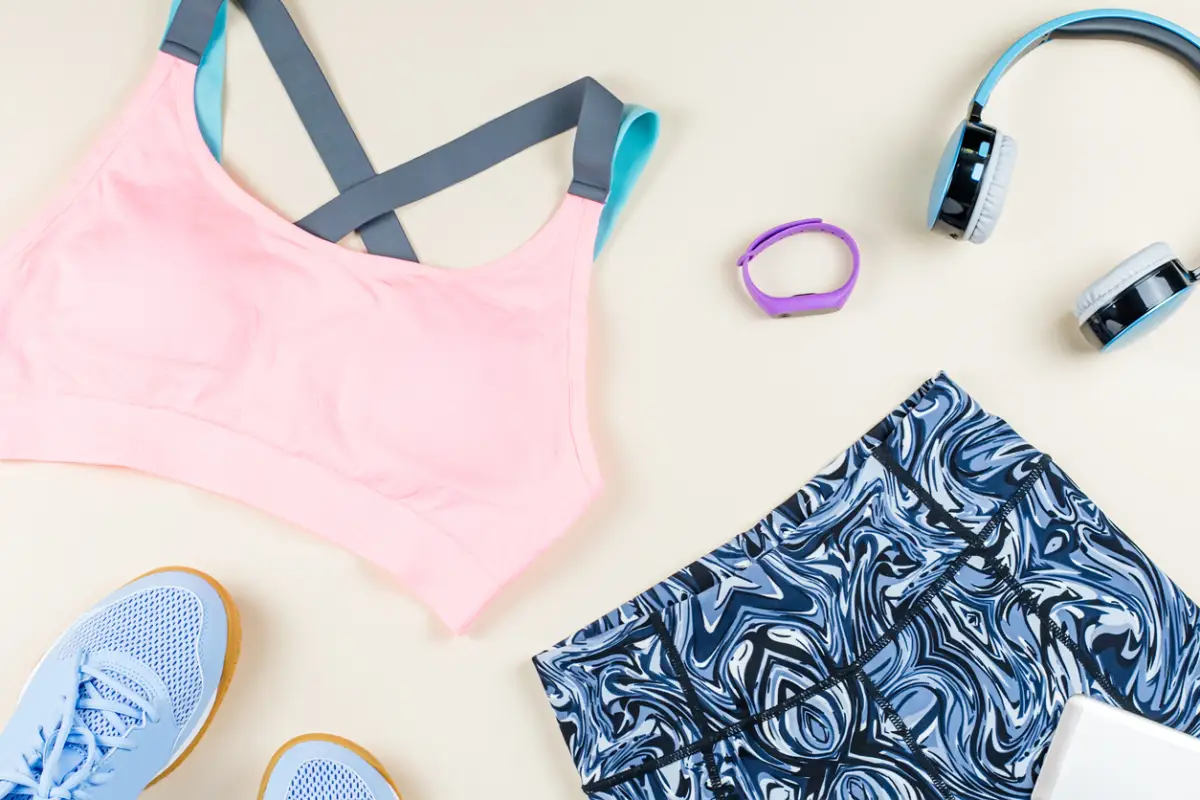 Woman sport bra, leggins, sneakers, headphones and fitness tracker on neutral background. Sport fashion concept.