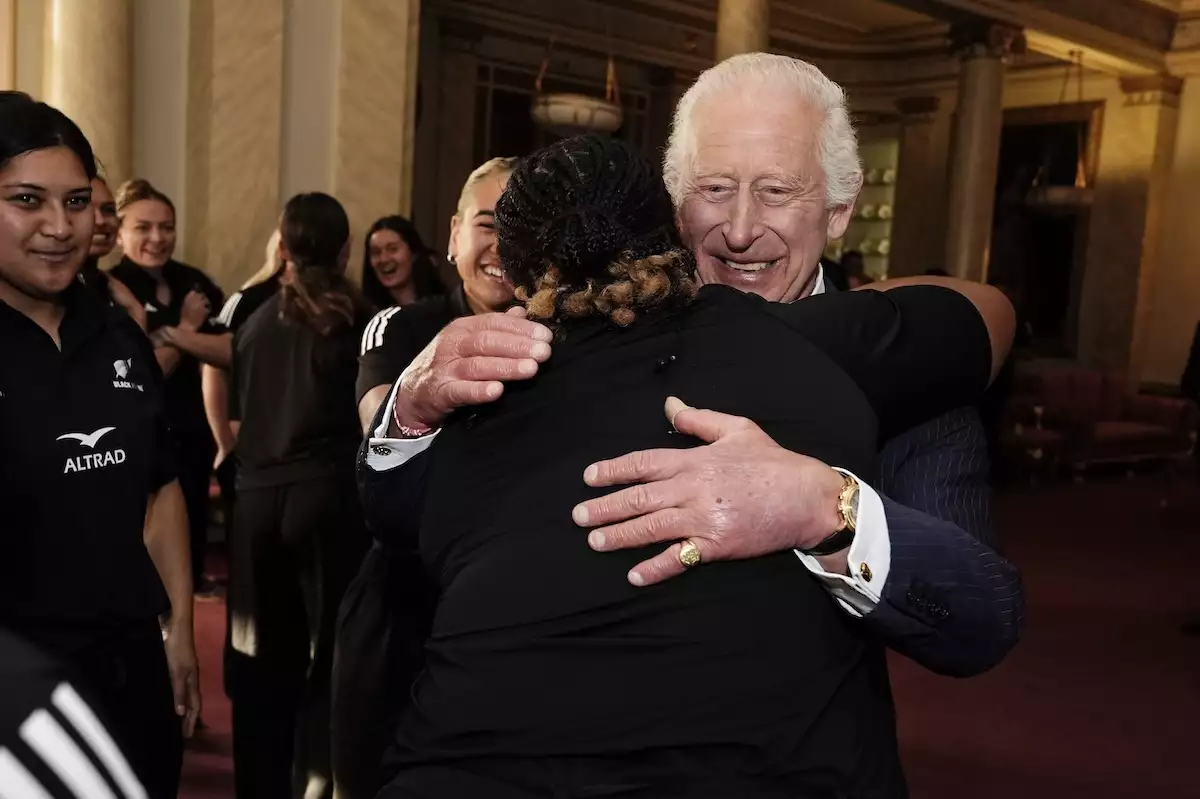 El rey Carlos III recibe un abrazo grupal del equipo de rugby femenil Black Ferns de Nueva Zelanda