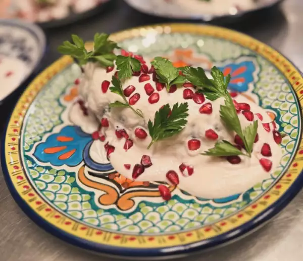 Foto de chile en nogada servido con la salsa (nogada) encima y granos de granada roja.
