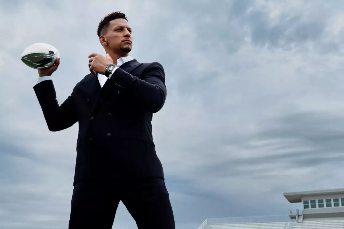 Foto de Patrick Mahomes en un traje negro lanzando un balón de futbol americano plateado.