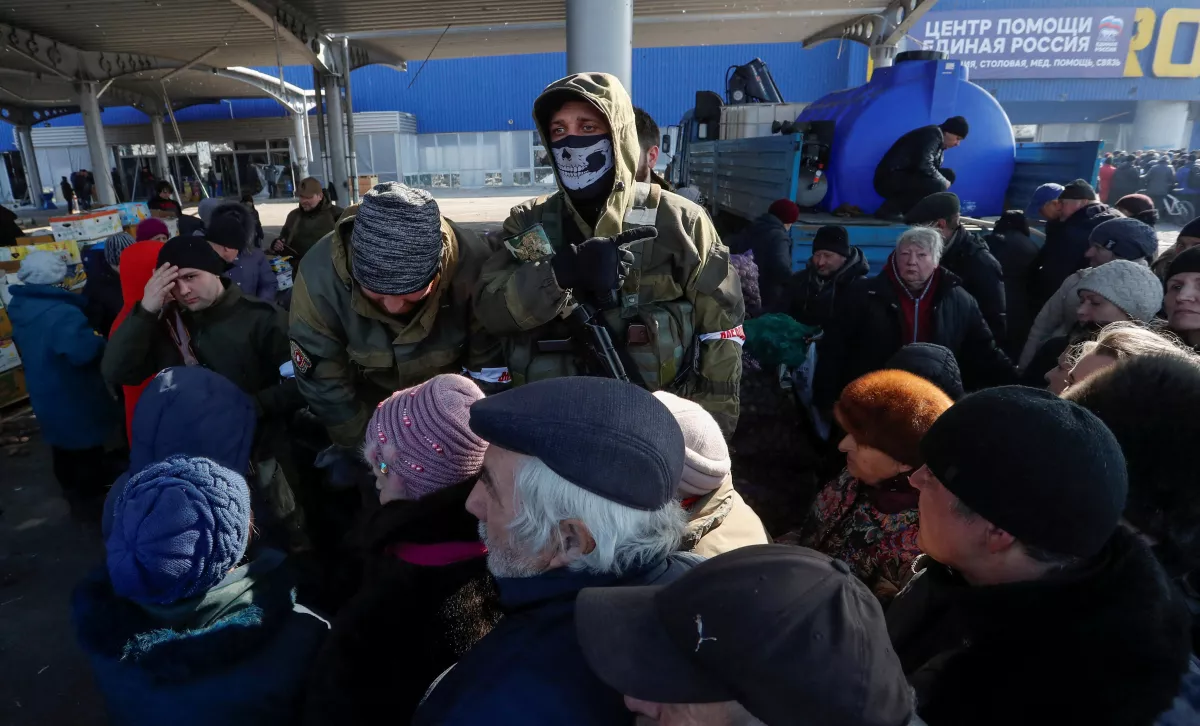 Miembros en servicio de tropas prorrusas hacen guardia mientras personas reciben ayuda humanitaria cerca de una tienda dañada en la ciudad sureña de Mariupol, Ucrania. 