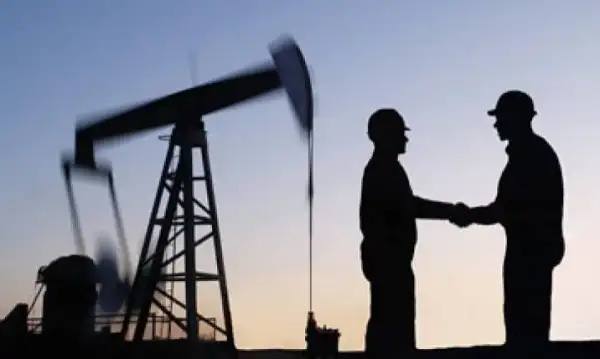 Dos hombres se saludan de mano frente a una refinería de petróleo. 