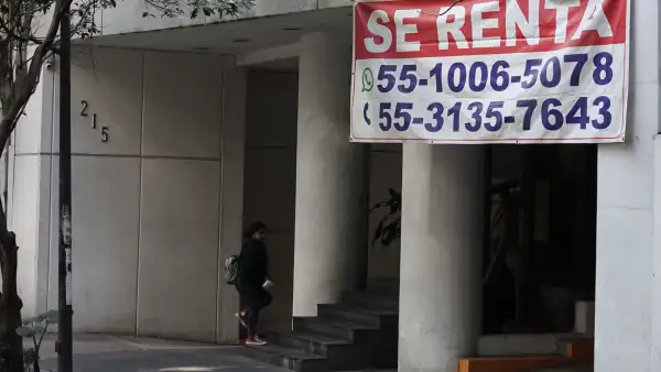 Una persona entra a un edificio del cual cuelga una gran lona con el anuncio 'se renta'.