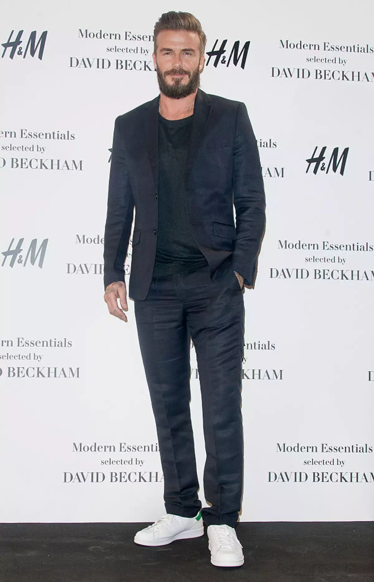 Foto de David Beckham con traje oscuro y tenis blancos en la presentación de su colección para H&M en 2015.