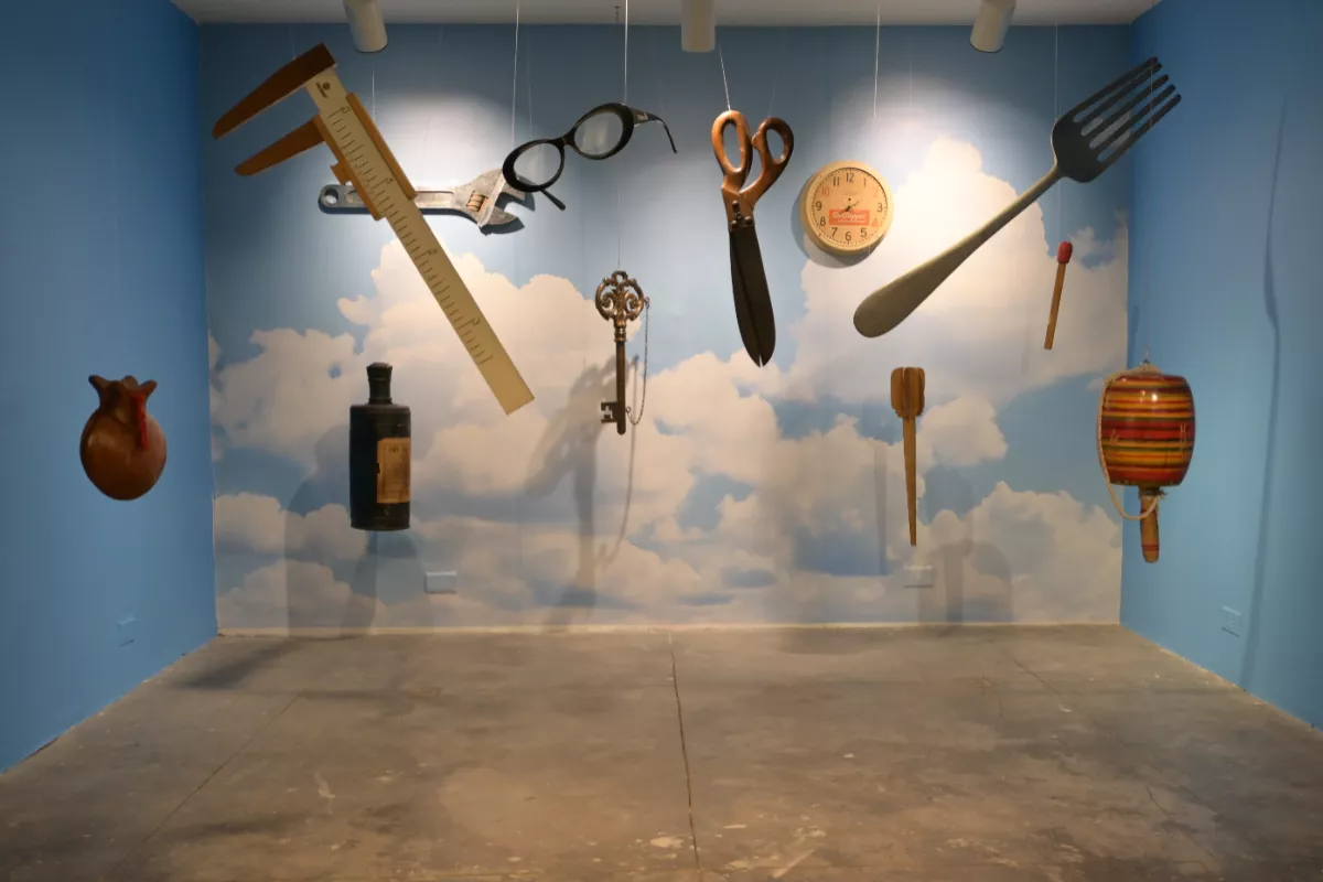 Foto de una gran sala con objetos comunes -como un tneedor, un balero, lentes o escuadras, hechos a gran escala y colgando del techo.