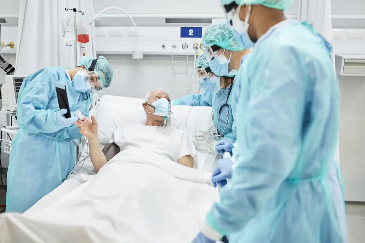 Médico mostrando la tableta digital al paciente en la sala después del tratamiento. Trabajadores de primera línea con monos protectores. Están en el hospital durante la COVID-19.