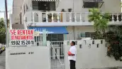 Un hombre parado frente a una casa con un letrero que dice "se rentan departamentos". 