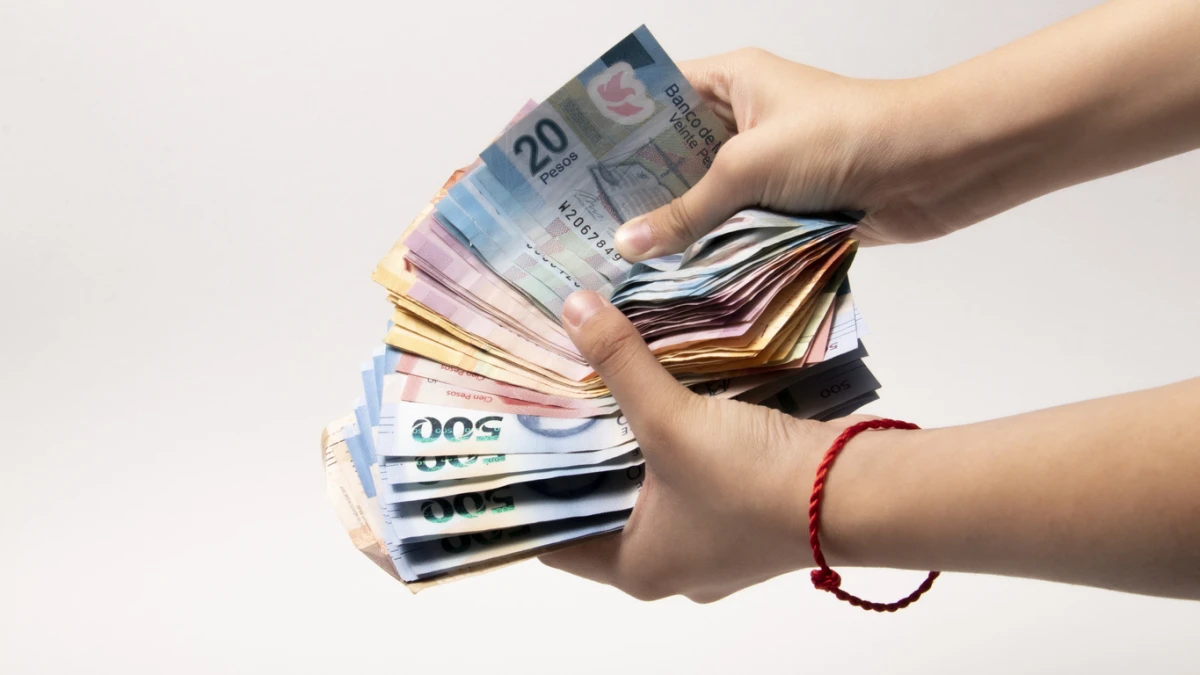 Cuánto es el máximo que puedes pagar en efectivo sin declarar ante el SAT (dos manos sostienen un fajo de billetes mexicanos)