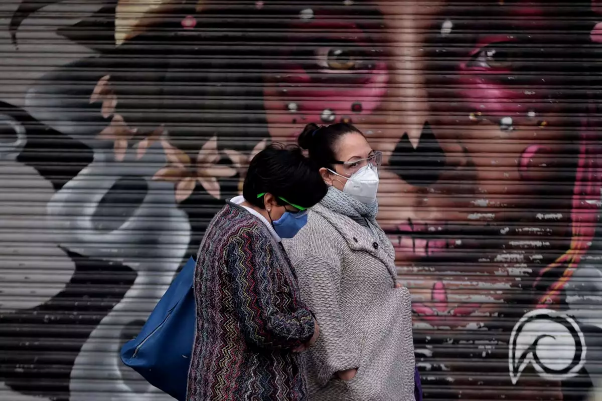 México suma 716 casos de Covid en 24 horas (Mujeres portando cubrebocas, pasan frente a la imagen de una catrina)