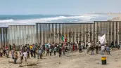 Dozens of migrants and workers on the sides of the US-Mexico border wall in Tijuana Beach