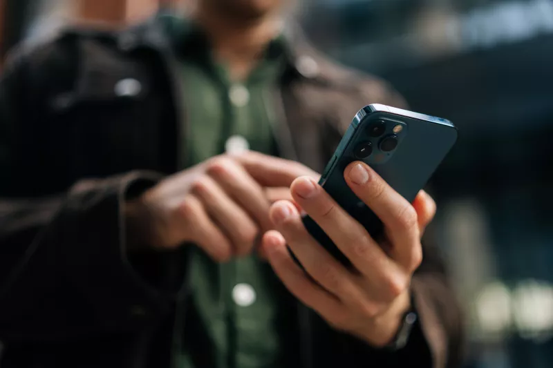 Close-up hands of unrecognizable man holding and using smartphone standing on city street, browsing internet, checking social media, using mobile application.