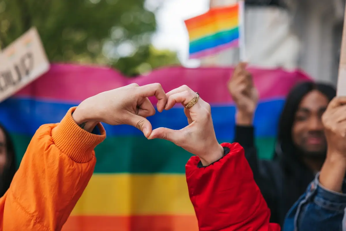 Manos forman un corazón frente una bandera LGBTQ+ durante una marcha del día del orgullo gay. 