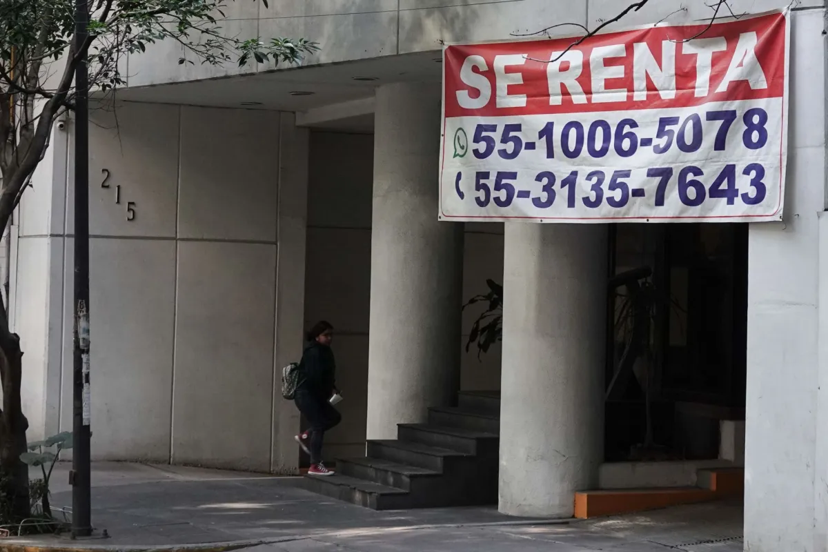 Una persona entra a un edificio del cual cuelga una gran lona con el anuncio 'se renta'.