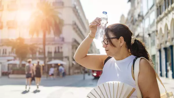Woman tourist walking by the city in a sunny summer day suffering from high temperatures, heat stroke and dehydratation