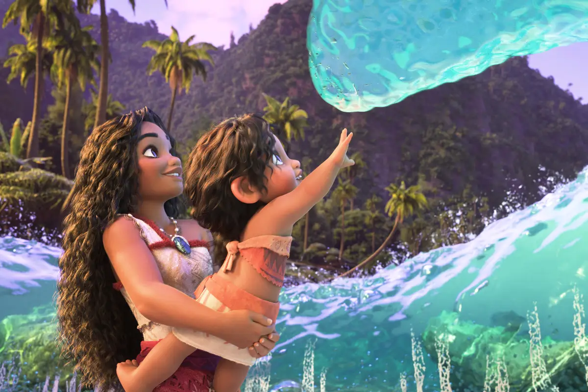 Foto de una escena de Moana 2, con la princesa cargando a un bebé en brazos, y el pequeño intenta alcanzar con su mano el agua del mar.