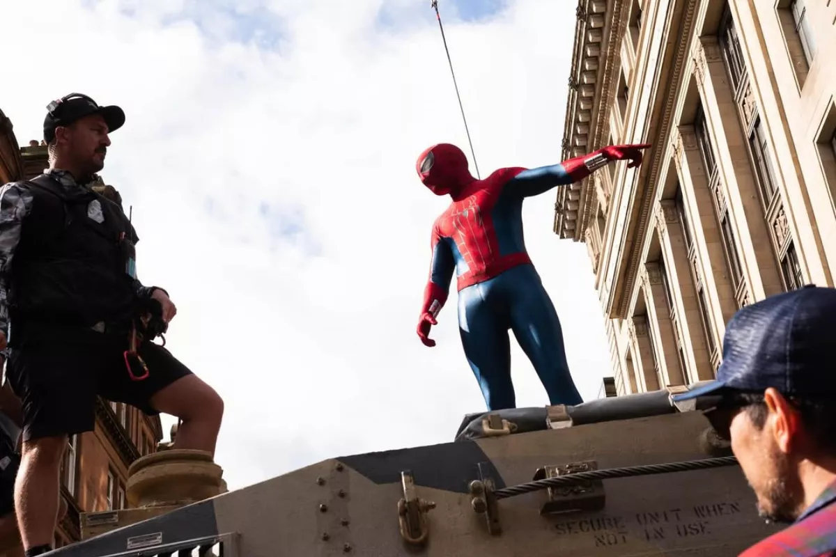 Foto de Tom Holland vestido como Spiderman sobre una estructura metálica, señalando con el dedo hacia un costado mientras habla con un integrante del equipo de producción.