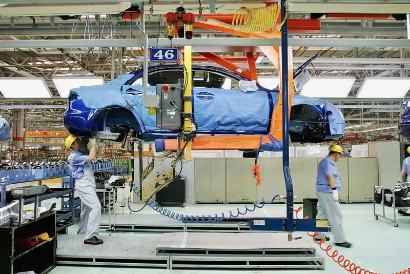 Una línea de ensamble de autos chinos en donde se ve como dos trabajadores ensamblar componentes.
