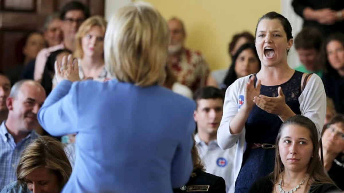 Hillary Clinton (de espaldas) es interrumpida durante una audiencia pública por varias personas, como la mujer de la derecha