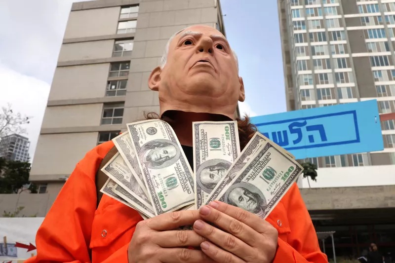 Manifestantes escenifican al primer ministro israelí, Benjamin Netanyahu, vestido con un mono naranja mientras recibe dinero de Qatar, ante el Tribunal de Distrito de Tel Aviv, el 9 de abril de 2025, donde Netanyahu debe testificar en el juicio contra él.