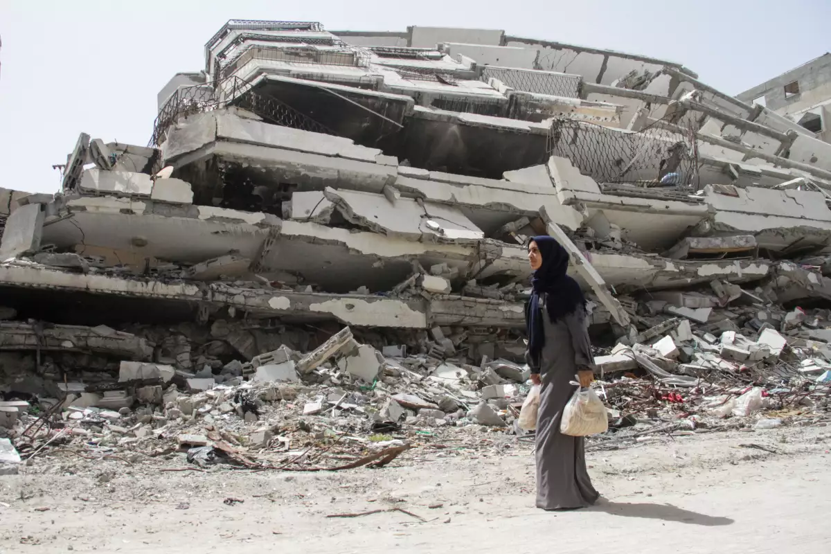 La mujer palestina Asmaa Al-Belbasi, regresando a su refugio después de comprar pan en la recientemente reabierta panadería Al-Sharq, pasa junto a las ruinas de una casa destruida durante la ofensiva militar de Israel, en medio del actual conflicto entre Israel y Hamas, en la ciudad de Gaza. 24 de abril de 2024.