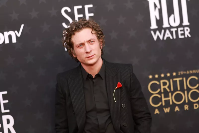 jeremy allen white protagonista de The Bear lleva un traje negro con camisa negra y un broche de una rosa roja a la alfombra roja de los Critics Choice Awards 2024