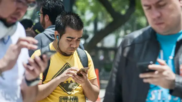 Tres personas sostienen sus teléfono celulares mientras caminan por la calle.