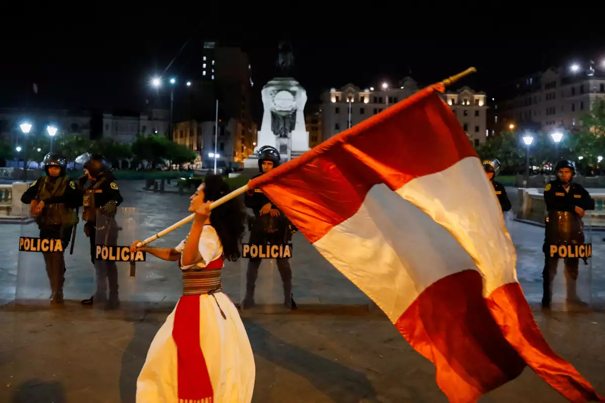 Las fuerzas de seguridad hacen guardia mientras un manifestante ondea la bandera de Perú durante una protesta para exigir la disolución del Congreso y elecciones democráticas, rechazando a Dina Boluarte como presidenta de Perú, luego del derrocamiento del presidente izquierdista Pedro Castillo, en Lima, Perú, el 12 de enero de 2023.