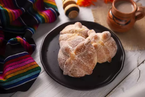 Pan de muerto en un altar, con una taza y rebozo a su lado.