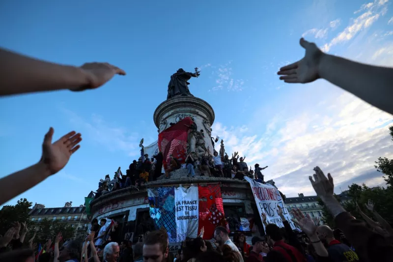 Los participantes hacen un gesto hacia una pancarta gigante que dice "Francia es el tejido de la migración" durante un mitin nocturno de las elecciones después de los primeros resultados de la segunda vuelta de las elecciones legislativas de Francia, en la Place de la Republique en París, el 7 de julio de 2024. Una alianza suelta de partidos franceses de izquierda unidos para elecciones anticipadas estaba en camino de convertirse en el bloque parlamentario más grande y vencer a la derecha, según los resultados proyectados de choque.