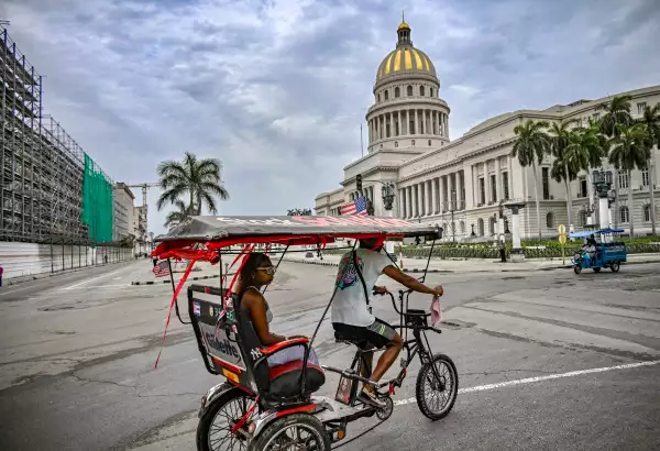 Un taxi en bicicleta decorado con una bandera estadounidense pasa frente al Capitolio de La Habana el 11 de julio de 2026. Cuba sufrió su segundo apagón nacional en cinco días el 10 de julio cuando las crisis energéticas y económicas gemelas, agravadas por un bloqueo de combustible estadounidense de seis meses, causaron el colapso de la red eléctrica.