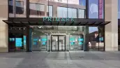 Entrada de una tienda Primark, en la que se muestran aparadores con ropa y zapatos de colores neutros como gris y nude. La fachada es color azul, con el nombre de la cadena en el mismo color en la parte de arriba de la entrada.

