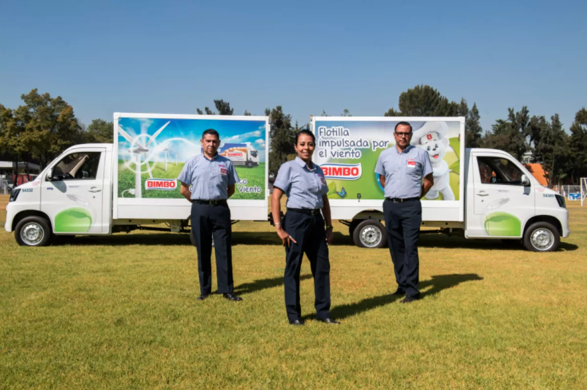 Se observan tres trabajadores de Bimbo frente a dos camiones de reparto. Grupo Bimbo, osito bimbo, mi ahorro bimbo