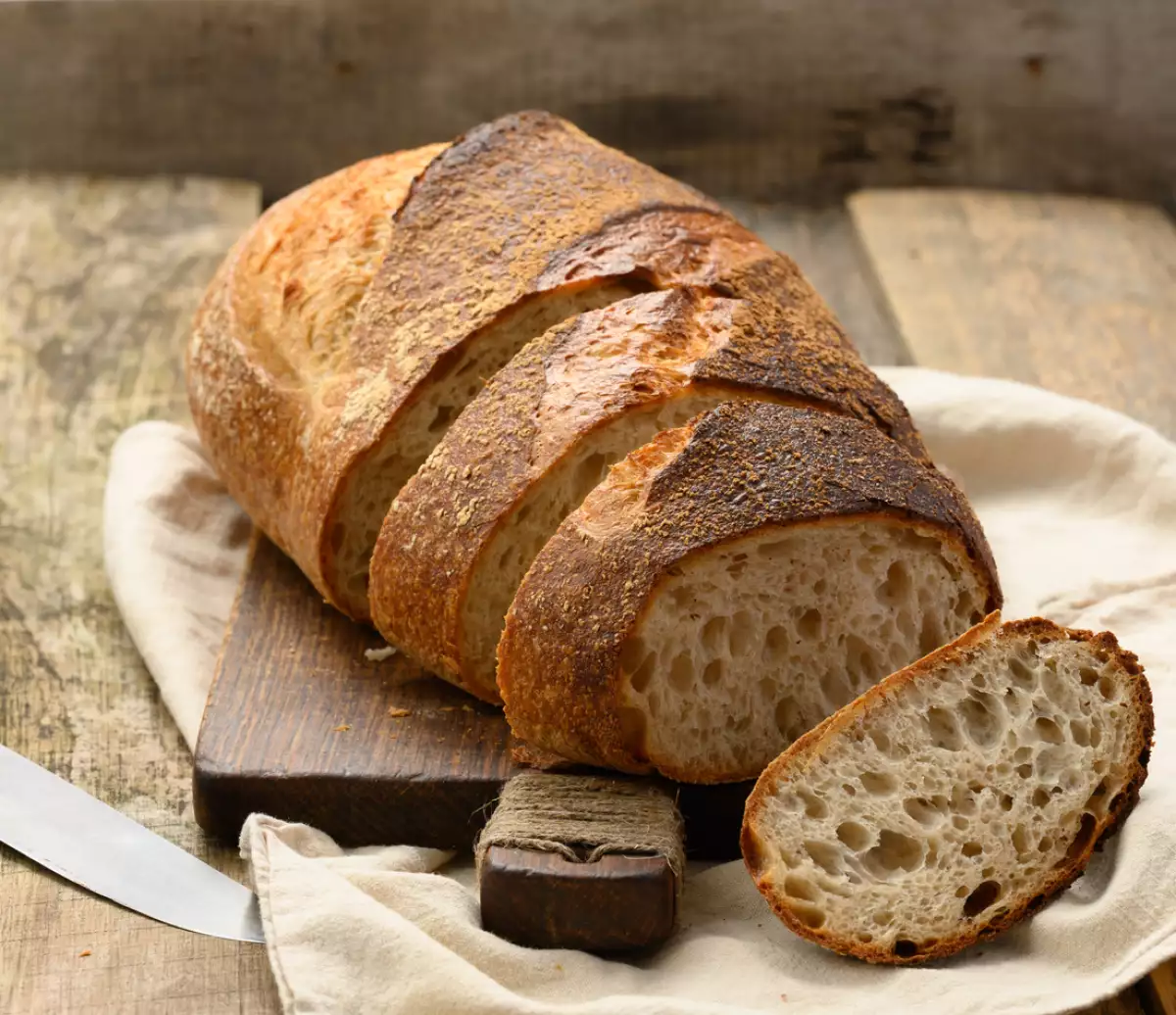baked round bread made from white wheat board on wooden board, loaf cut into pieces