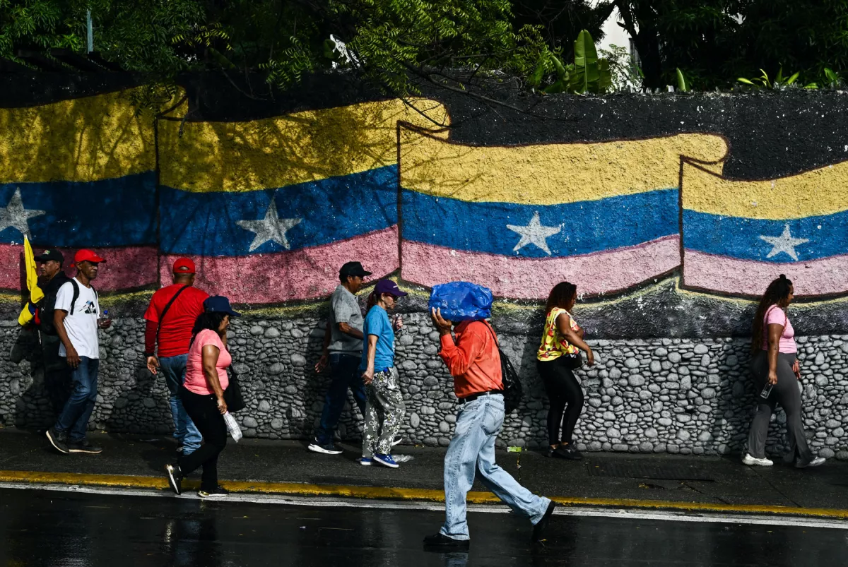 La gente se para frente a un mural con una bandera venezolana en Caracas el 7 de enero de 2026. La administración del presidente de los Estados Unidos, Donald Trump, dijo el 7 de enero que tiene la intención de dictar las decisiones de los líderes interinos de Venezuela y controlar las ventas de petróleo del país "indefinidamente" después de derrocar a Nicolás Maduro.