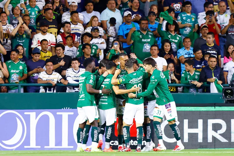 Foto de jugadores del Club León abrazándose en el campo del Estadio León frente a aficionados que les aplauden.