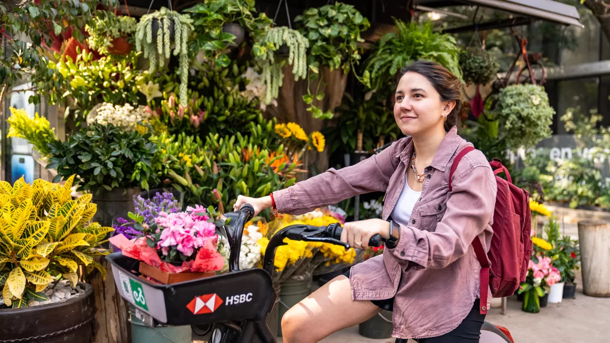 Mujer paseando en Ecobici por un lugar donde hay flores.
