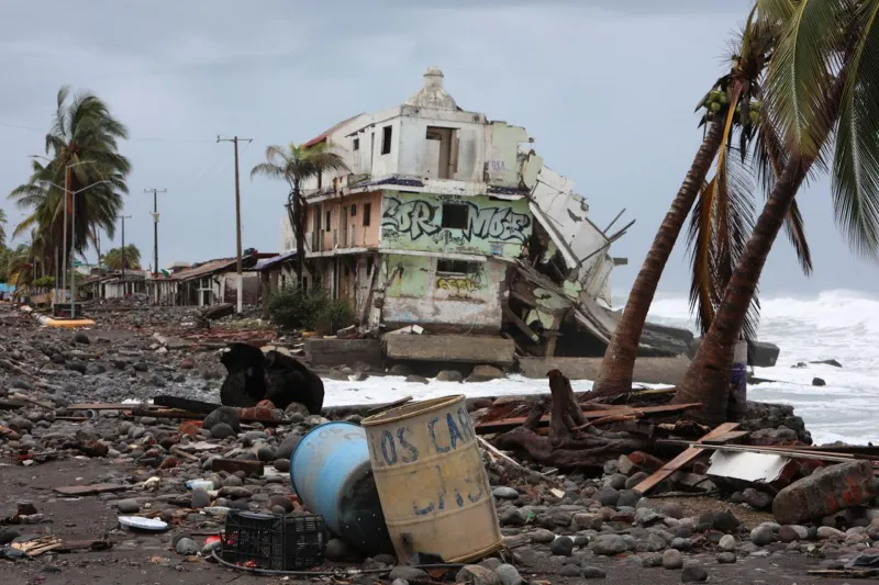 En la imagen se observa una vivienda destruida por el paso del huracán Simón en Colima, así como palmeras dañadas y basura arrastrada a la orilla del mar.