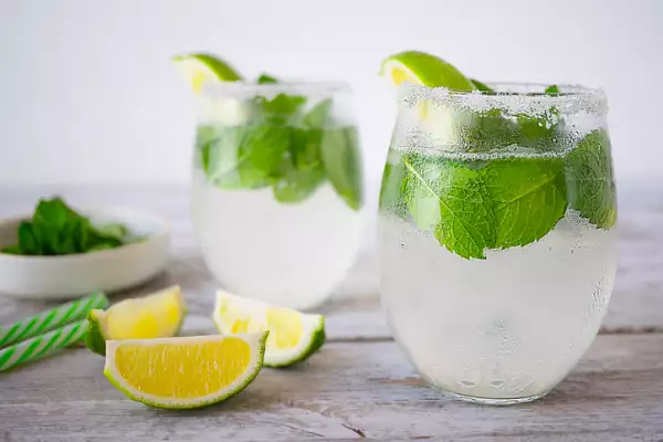 Dos vasos con rodajas de limón, popotes y plantas de menta.