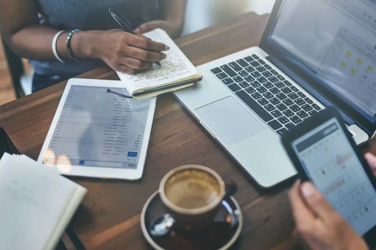 Personas planeando  estrategias de marketing digital: unas toma nota en una libreta, otro revisa en su celular y ven una pantalla de una laptop.