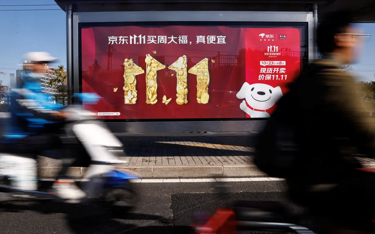La gente viaja en un scooter más allá de un anuncio de JD.com que promueve el festival de compras Singles Day, en Beijing, China, el 26 de octubre de 2023.