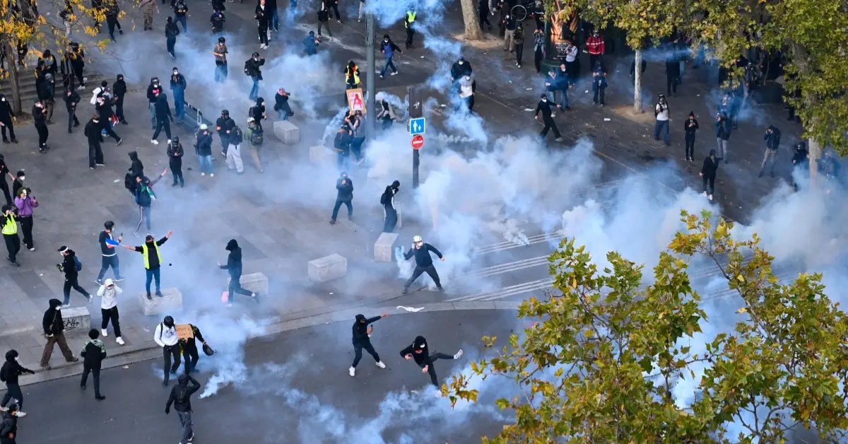 Grupos de jóvenes en medio de gases lacrimógenos en una plaza donde hay árboles.jpg