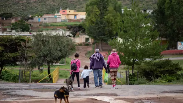 Una familia compuesta por hombre mujer y dos niños caminan de espaldas alejándose. En primer plano hay un perrito.