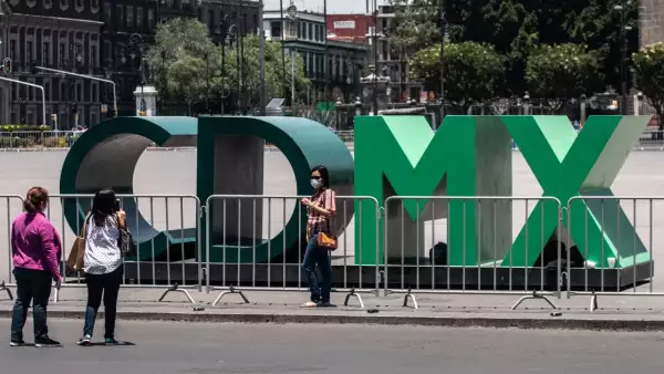 Turistas se toman una fotografía en las emblemáticas letras "CDMX" ubicadas en la Plancha del Zócalo Capitalino, la cual se encuentra cercada con vallas metálicas para evitar aglomeraciones