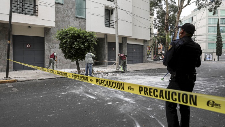City workers remove debris from a building facade as a police officer checks, after an earthquake was felt in Mexico City