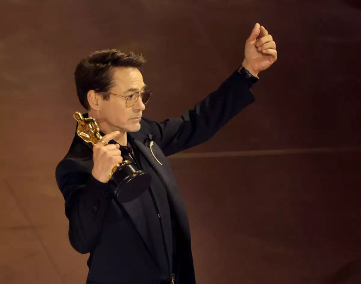 foto de robert downey jr de perfil con el oscar en la mano derecha y haciendo una señal de corazón coreano con la mano izquierda